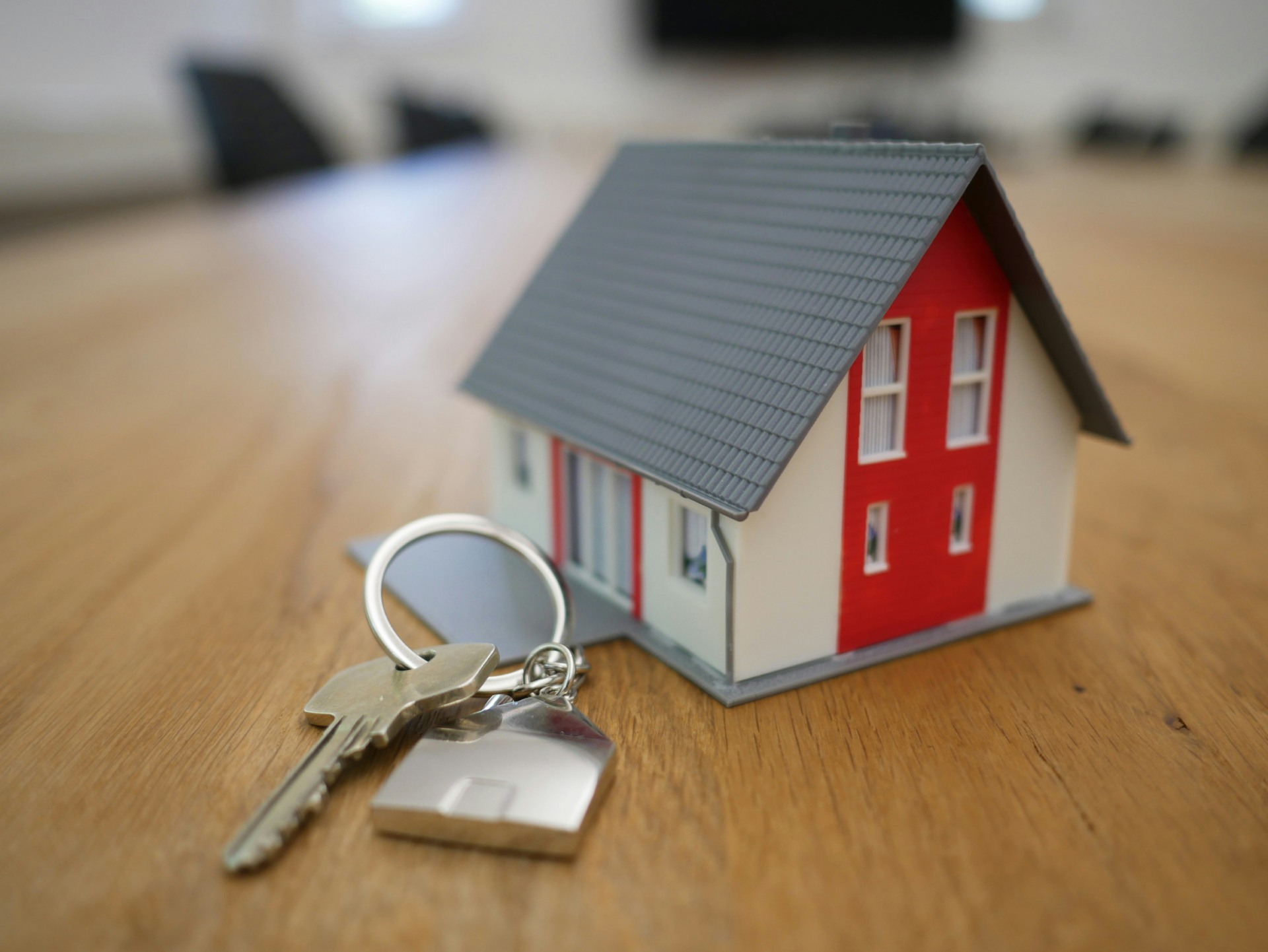 Model house with keys on a wooden table.